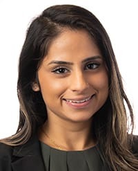 Panchal A woman with long, dark hair wearing a black blazer and dark top, smiling at the camera against a white background.